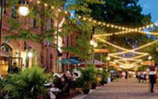 A set of of brick buildings and a brick path, tables for eating outside, lights strung between buildings, night scene